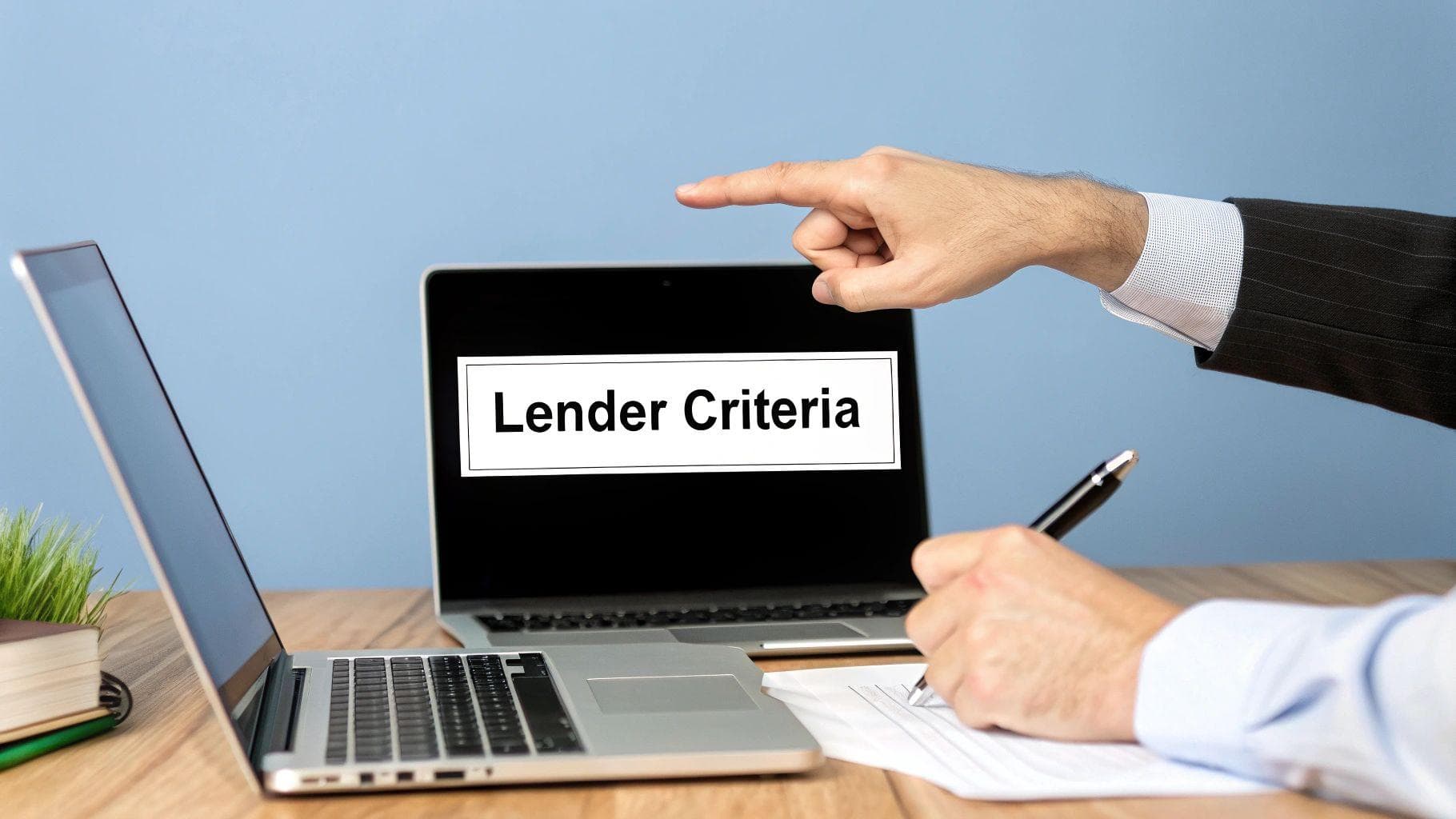 A person's hand points to a laptop screen displaying 'Lender Criteria' while another writes notes.